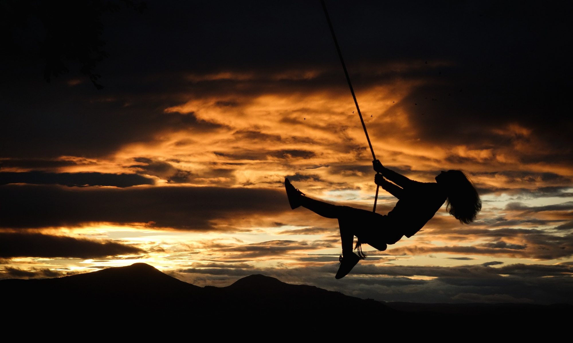A girl on a swing in front of a sunset